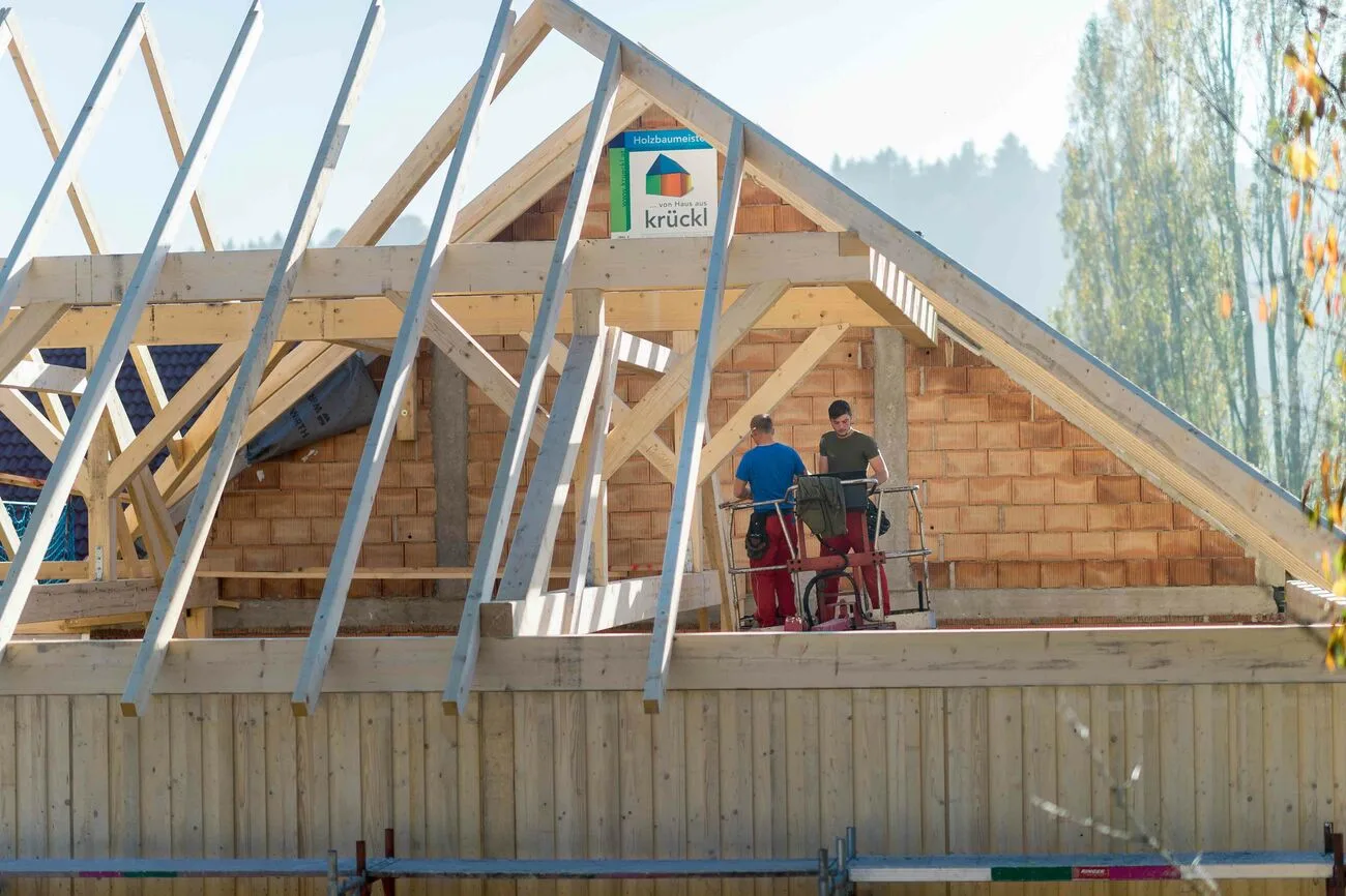 Rohbau mit neuem Dachstuhl aus Holz, an der Giebelseite die Bautafel mit dem krückl-Logo, zwei Arbeiter am Gerüst