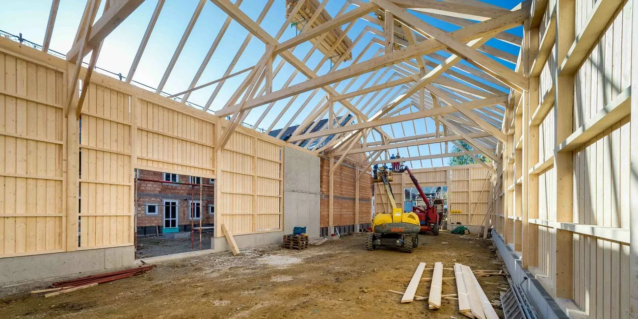 Innenansicht einer Holzhalle im Bau mit Dachstuhl und Bagger