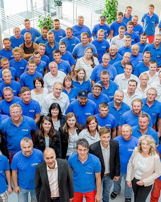 Die Belegschaft von Krückl Bau in blauen Firmenshirts im Atrium der Firmenzentrale