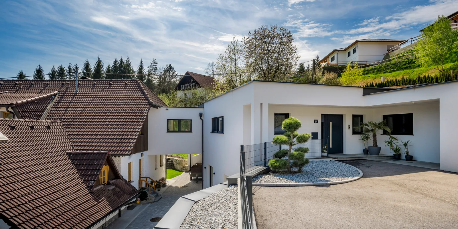 Weißes Wohnhaus mit Ziegeldach und gepflastertem Hof am Hang