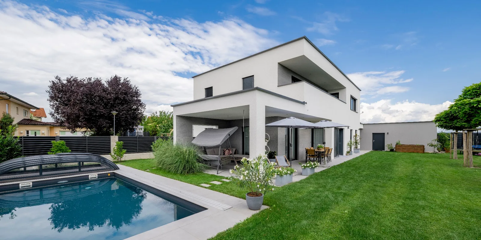 Weißes Einfamilienhaus mit Flachdächern, Terrasse, Rasen und überdachtem Pool
