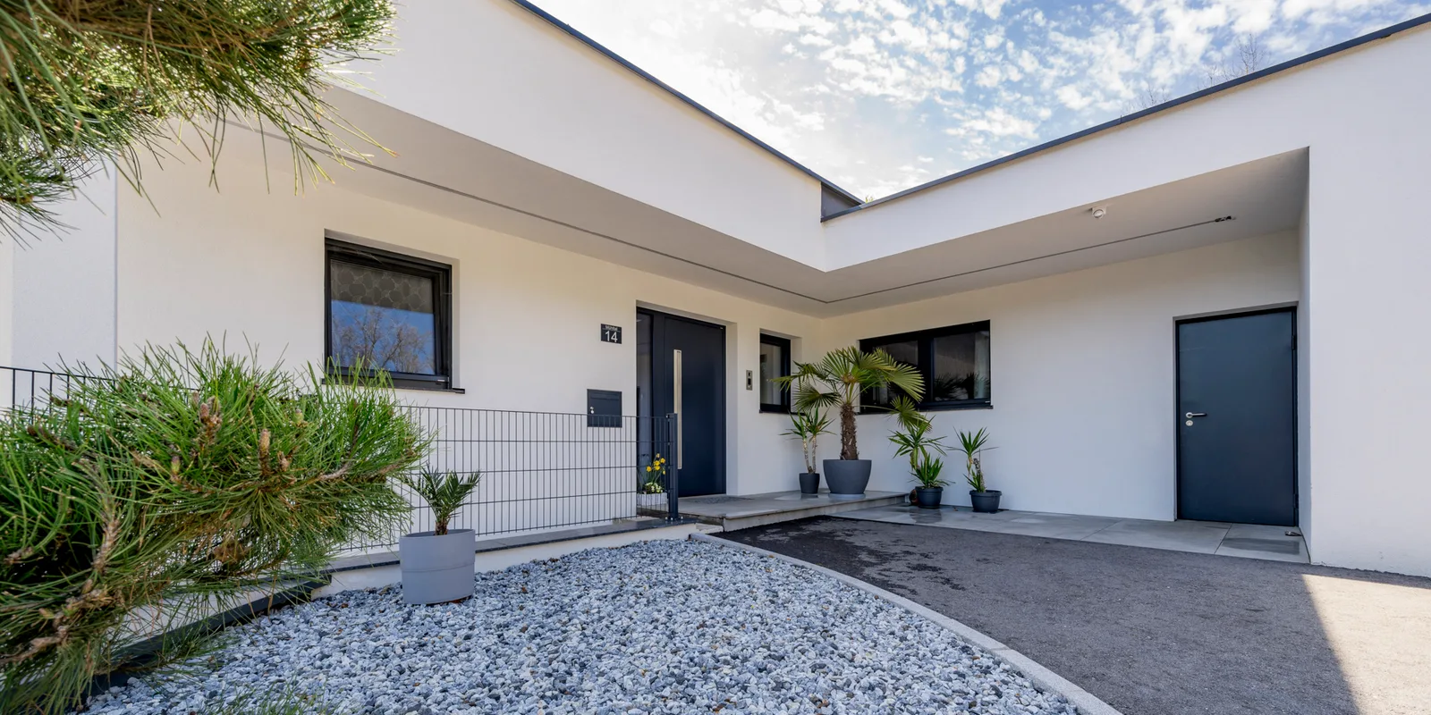 Weißer Winkelbungalow mit dunkler Haustür und Kiesbeet