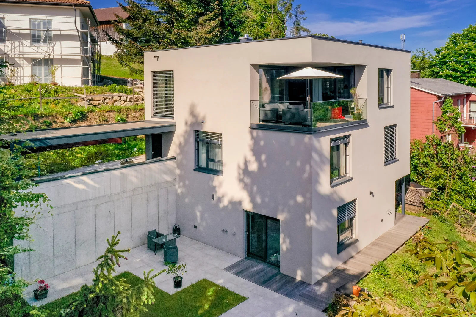 Dreigeschoßiges weißes Haus am Hang mit Balkon und Sonnenschirm