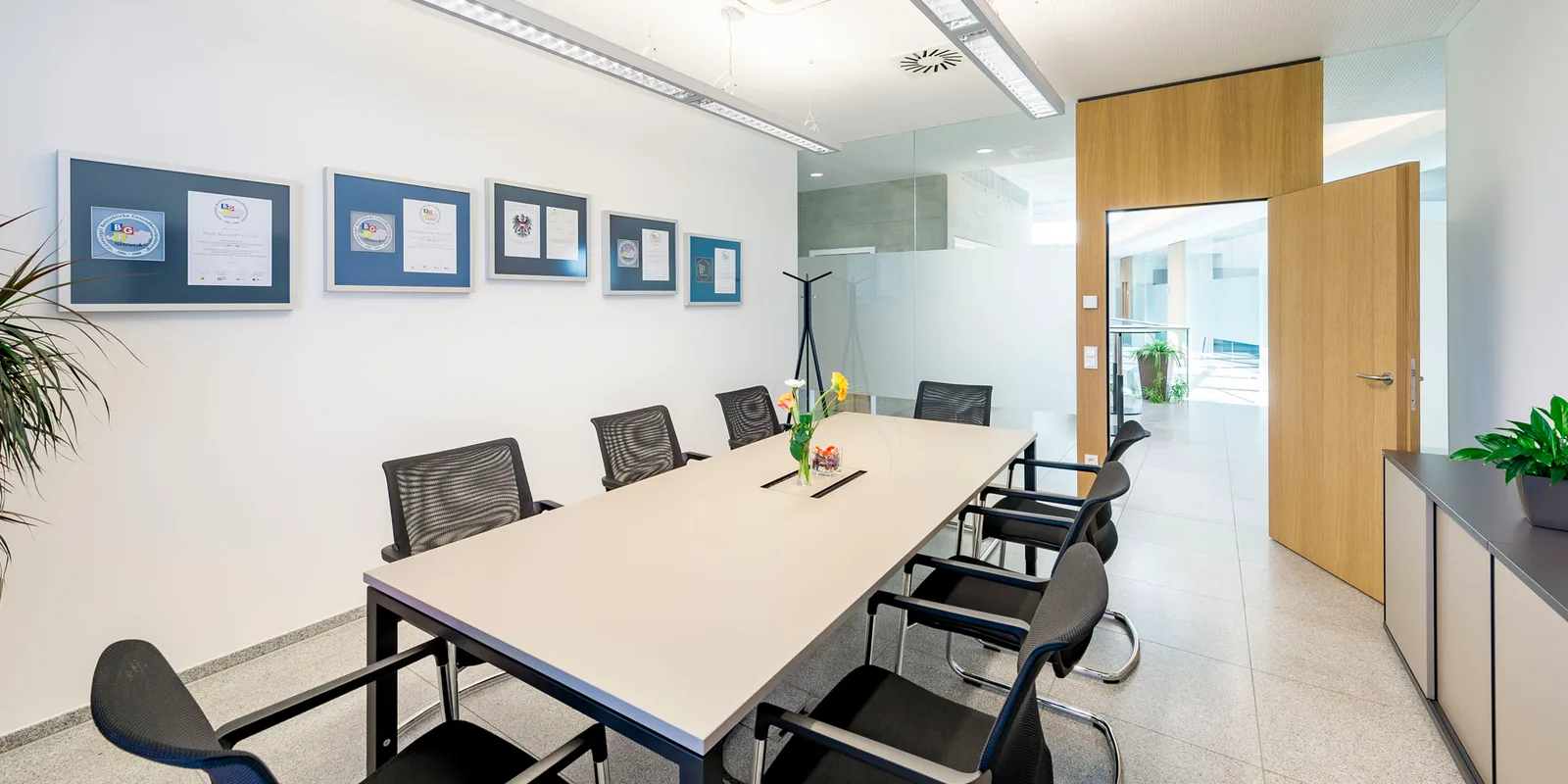 Besprechungsraum mit langem Tisch, an der Wand gerahmte Urkunden